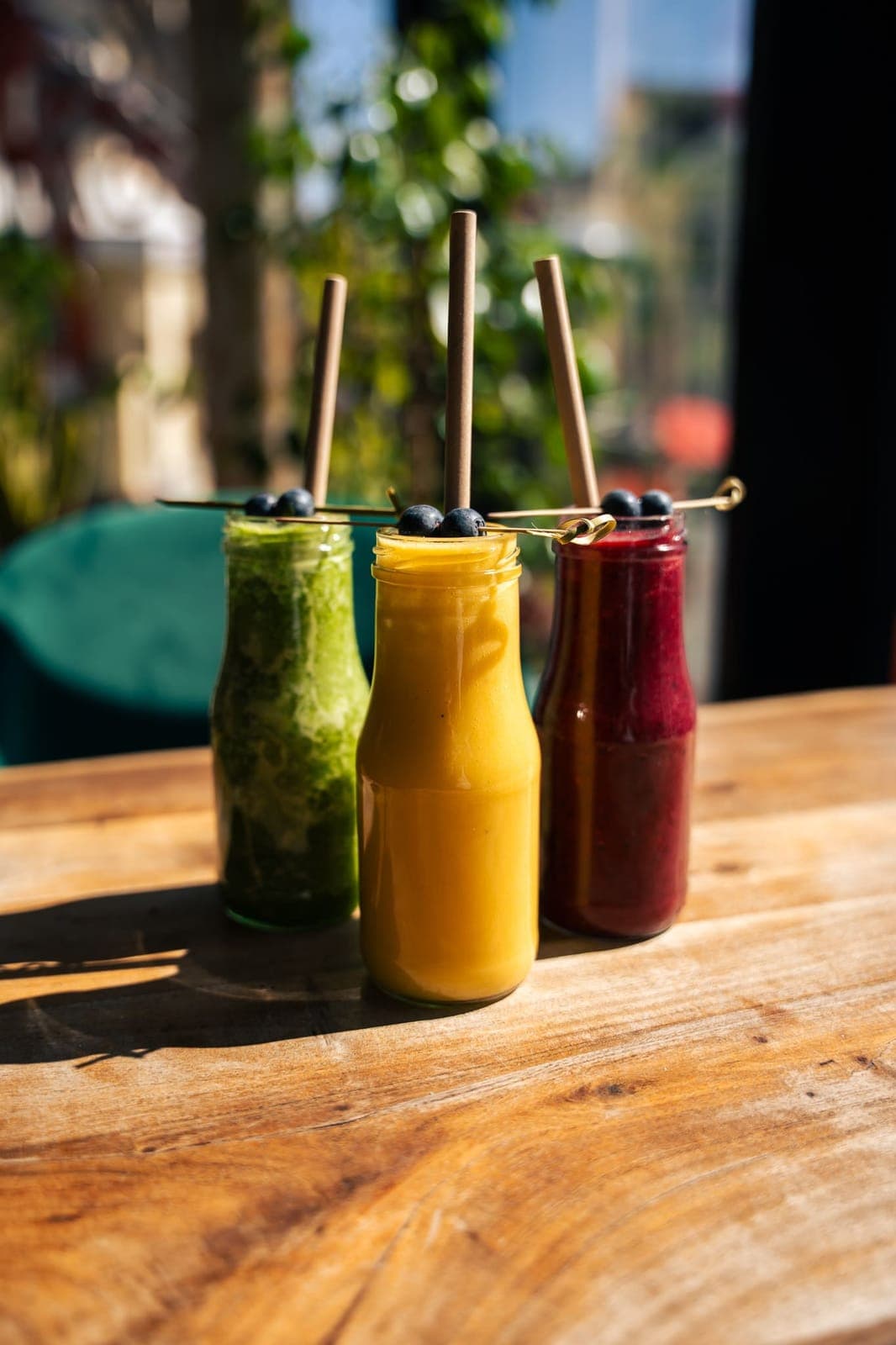 Drei Smoothies in Glasflaschen mit Blaubeeren am Strohhalm