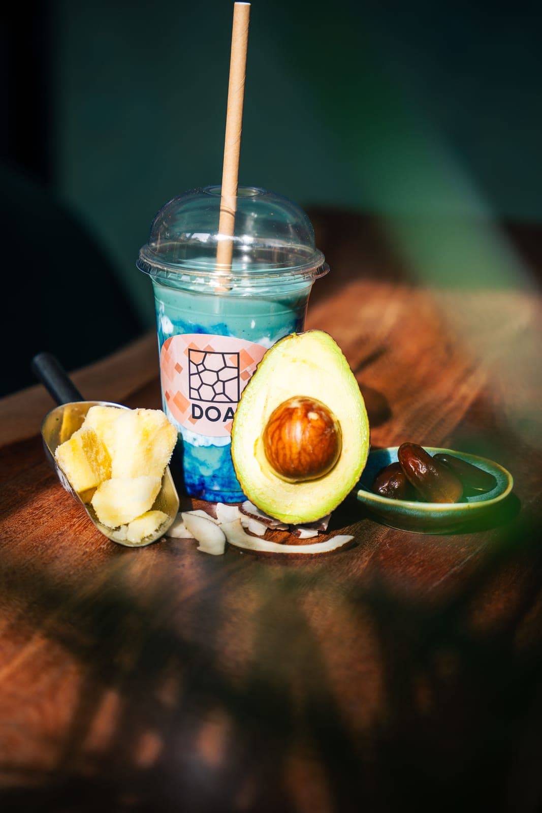 Blauer Smoothie im DOA-Becher neben aufgeschnittener Avocado